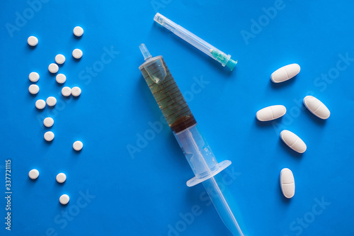 large and small pills scattered on a blue background and a syringe