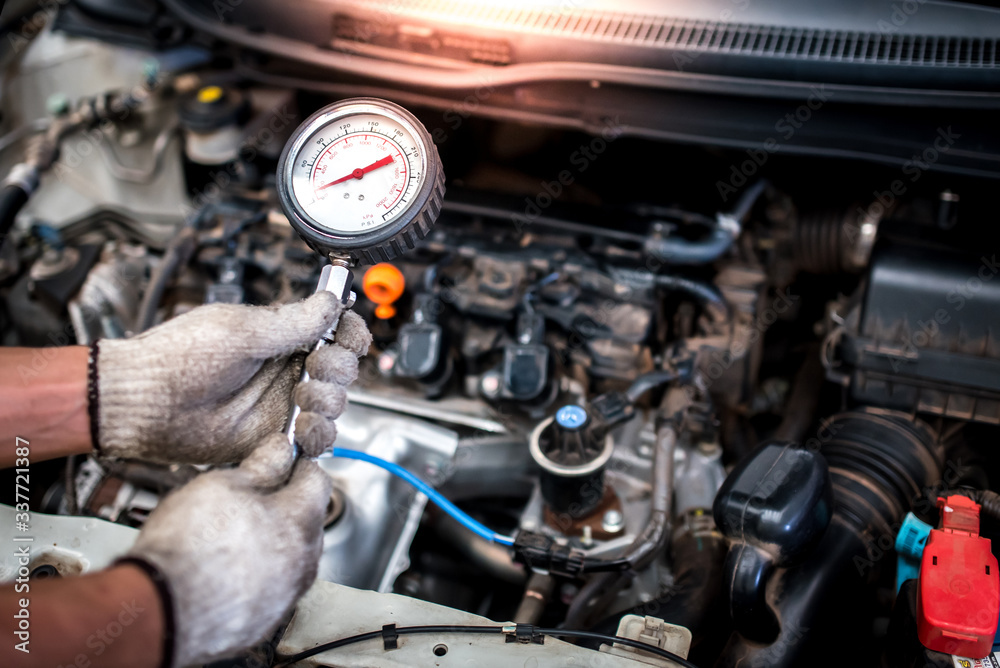 The auto mechanic is about to measure compression in the cylinder of a car engine using a