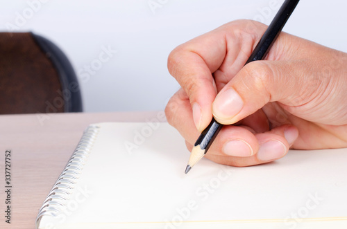 Close up of hand writing with pencil to notepad paper on working desk for business backgrounds