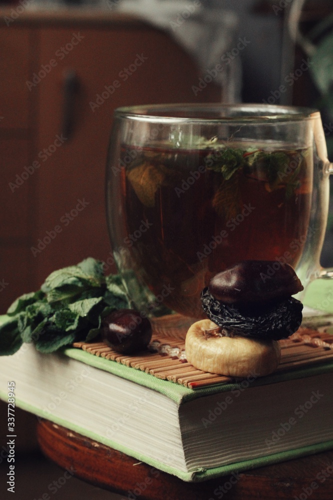 Dark mystic and calm mood. Book and hot tea with mint and honey on table with green plant