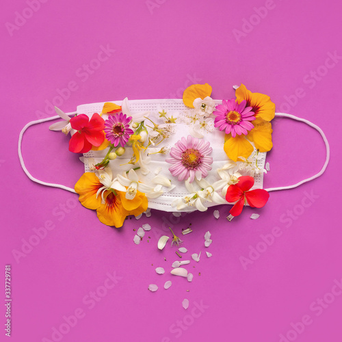white medical mask flowers on top with diffrent color flowers on pink background top view with.Coronavirus Covid quarantin concept win