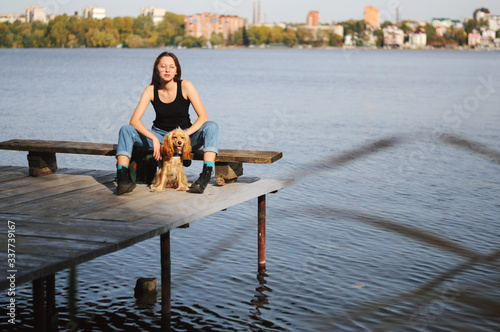 Girl with her dog, English Cocker Spaniel, sitting on the bench near the lake