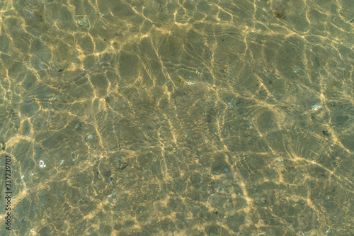 Sandy bottom with pebbles and reflection of waves on the surface of the water