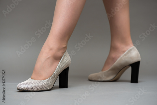 Female legs in pantyhose in high heel shoes close up on gray background.