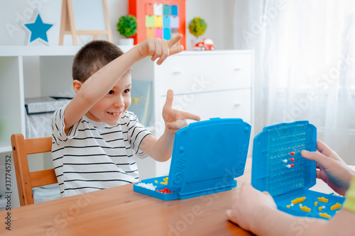 Boy child with dad playing warships and submarines are placed on the playing field in the game battleship. entertainment