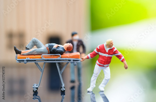 Miniature people : Injured man lying on the first aid bed and there is emergency medical staff dragging a first aid bed. Focus on emergency man. Emergency, life insurance, accident concept.