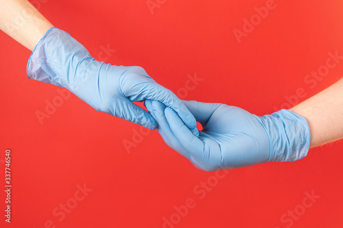 Two hands in blue medical gloves hold each other. Red background. Concept protection from a virus, pandemic, epidemic, disease. Minimalism, copyspace. Male and female hand.