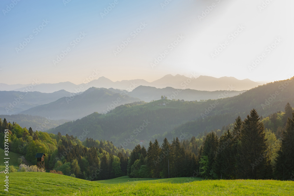 Slovenian breathtaking landscape at sunrise with Julian Alps and charming little church of Sveti Tomaz (Saint Thomas) on a hill, in spring. Beautiful misty morning in the mountains, in Slovenia.