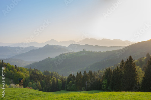 Slovenian breathtaking landscape at sunrise with Julian Alps and charming little church of Sveti Tomaz  Saint Thomas  on a hill  in spring. Beautiful misty morning in the mountains  in Slovenia.