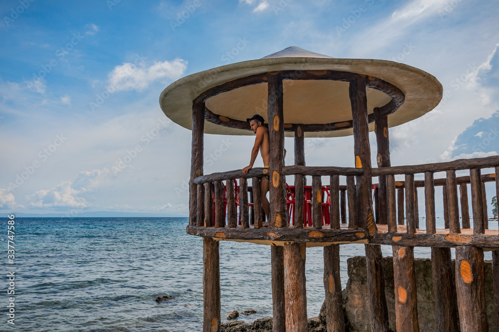 A young man standing on an outdoor terrace over the sea in Oslob, Philippines A young man standing on an outdoor terrace over the sea in Oslob, Philippines