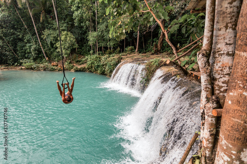 A young caucasian man plays with a rope swing over the Cambugahay Falls in Siquijor Island, Philippines photo