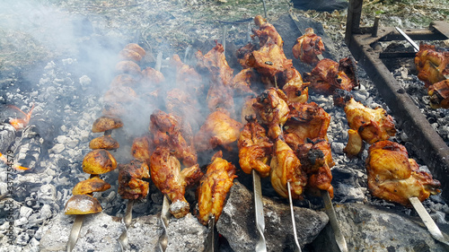 The chicken is fried on hot coals. Smoke and the smell of barbecue rises from the pieces of coal. Summer recreation environment in the forest. Tourist meals in the nature.
