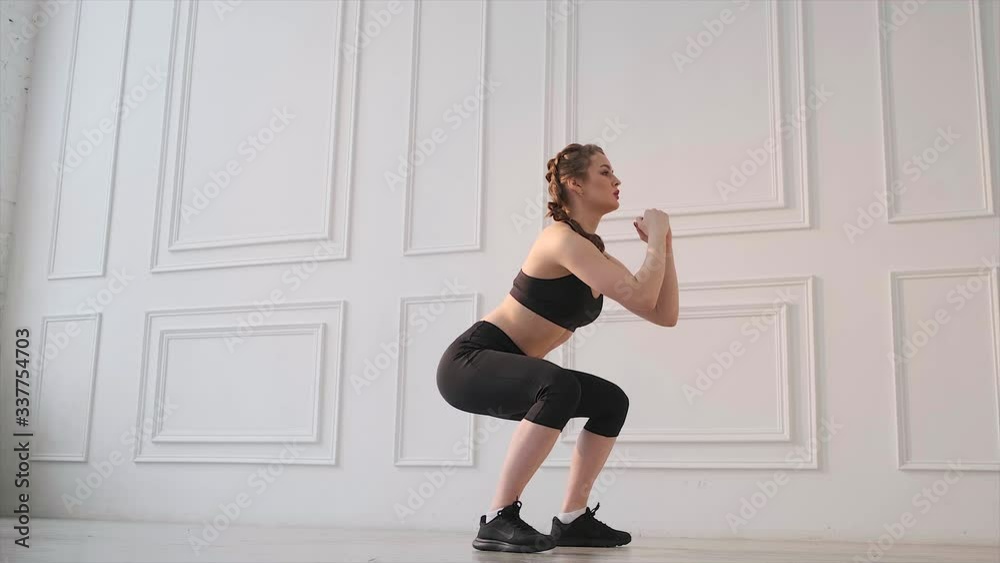 Girl in black suit on a white background does squats during workout sessions. Girl in black suit on a white background does squats during workout sessions.