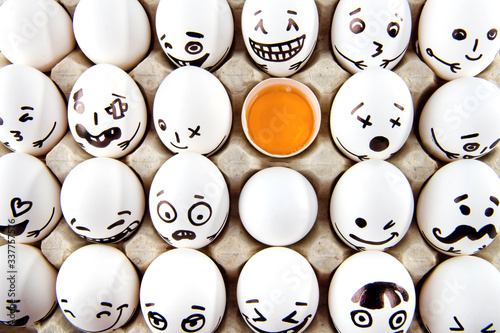 Eggs with drawn cartoon faces and one broken egg in tray. photo