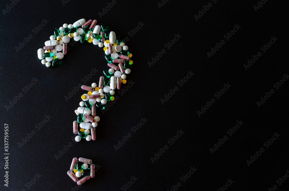 A question mark laid out of pills on the left side of the black matte background. photo with selective focus. Medical pharmacy background. Copy space.