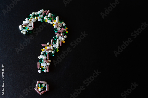 A question mark laid out of pills on the left side of the black matte background. photo with selective focus. Medical pharmacy background. Copy space.