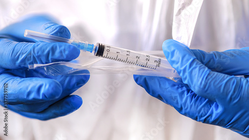A doctor in blue rubber gloves unpacks a disposable sterile medical syringe.