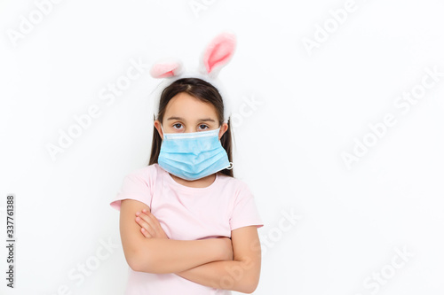 Little caucasian girl with bunny ears and medical mask on her face on a white background. Easter concept. Coronavirus protected © Angelov