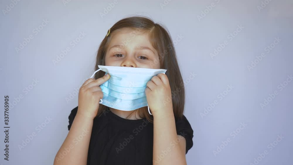 A child girl wears a protective medical mask against bacteria and viruses by herself. Stock video. A child girl wears a protective medical mask against bacteria and viruses by herself. Stock video.