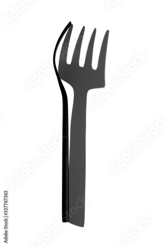 Black fork with a hard shadow on a bleached background top view.