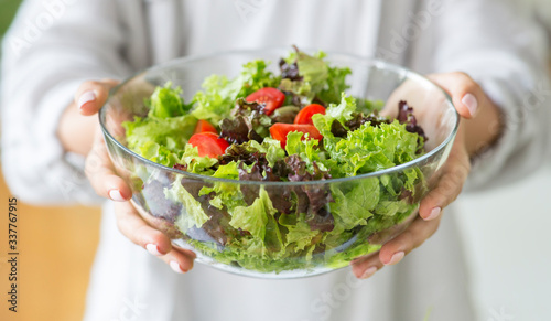 Woman preparing healthy salad in big glass bowl in the kitchen