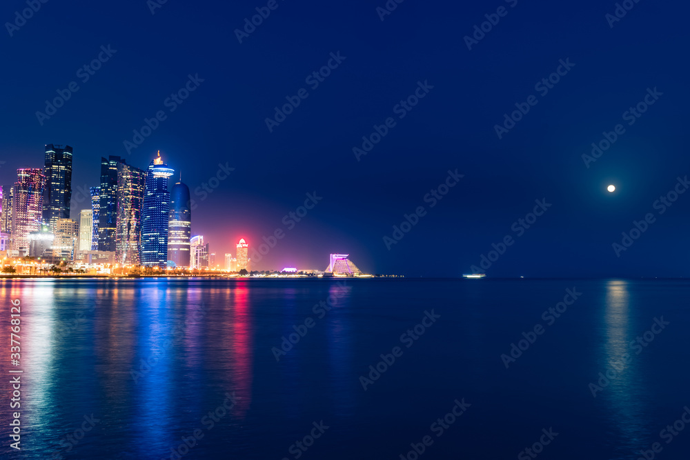 Night view on the centre of the city Doha, Qatar and the Gulf with the moon shining and many modern luxury building and skyscrapers