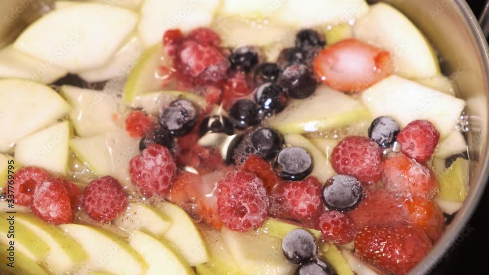 Cooking sweet delicious healthy homemade compote drink from tasty apples and frozen berries in a steel sauce pan Cooking sweet delicious healthy homemade compote drink from tasty apples and frozen berries in a steel sauce pan