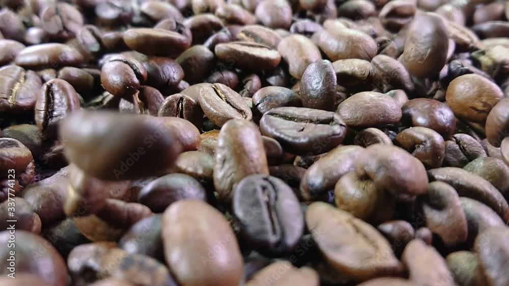Close-up view of roasted coffee beans falling down on the pile of coffee beans in slow motion Close-up view of roasted coffee beans falling down on the pile of coffee beans in slow motion