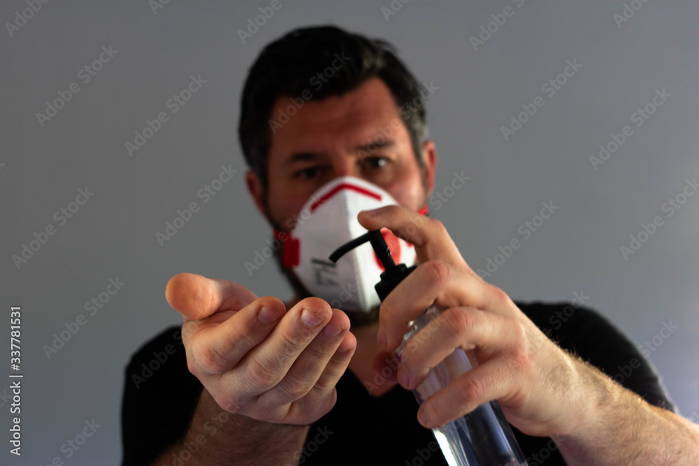 Man wearing a FFP3 hygiene mask to protect against corona virus while using hand sanitizer Man wearing a FFP3 hygiene mask to protect against corona virus while using hand sanitizer