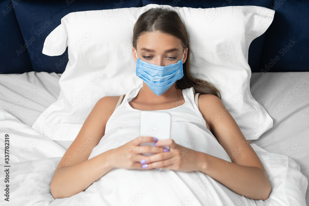 Lady In Protective Medical Mask Using Cellphone Lying In Bed