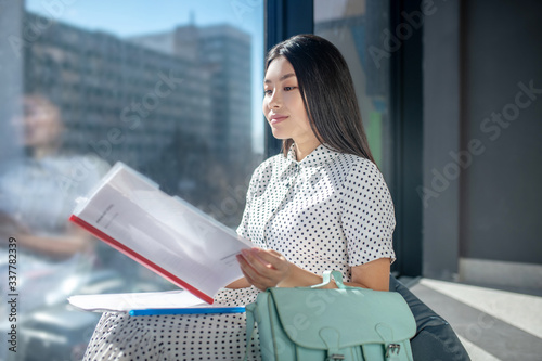 Pretty young dark-haired businesswoman looking serious and looking through the documents photo