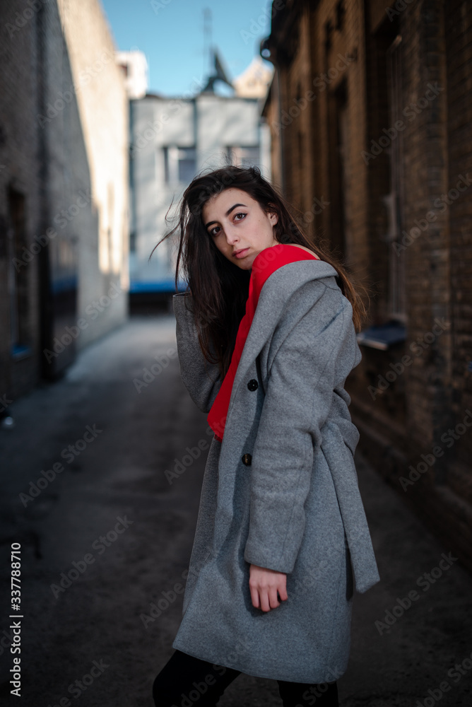 Girl in a red blouse and a gray cardigan on the background of the old brick wall