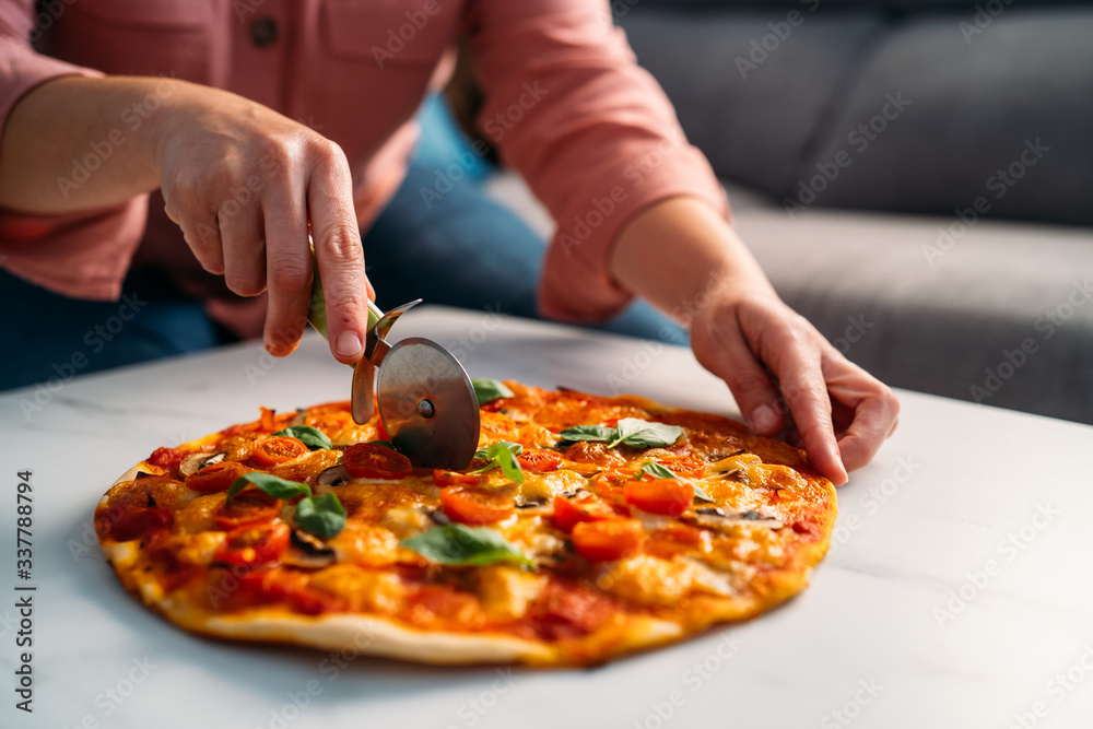 Woman cutting a traditional italian margarita pizza in her living room. Stay at home
