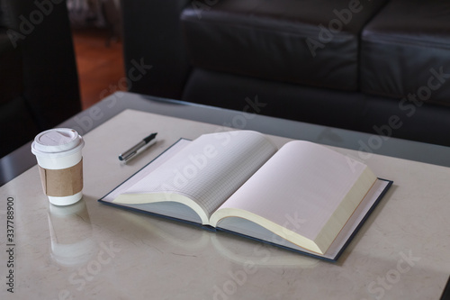 Open notebook with pen and a disposable coffee cup over glass table