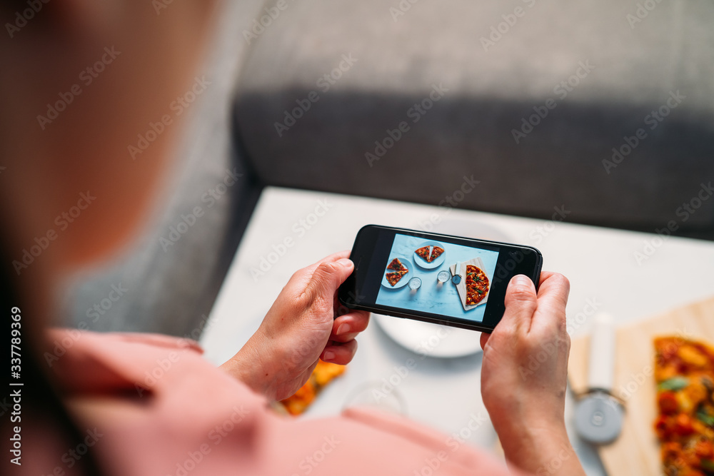Woman making a photo with smartphone of a Italian homemade pizza on the living room table