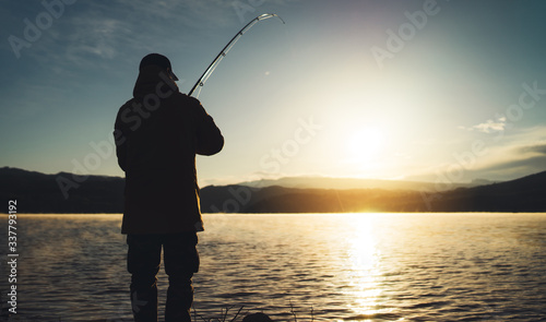 silhouette fisherman with fishing rod at sunrise sunlight, outline man enjoy hobby sport on evening lake, person catch fish at night sky, relaxation fishery concept
