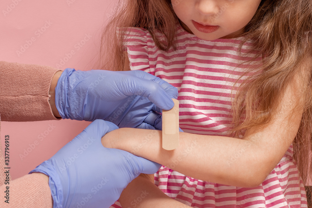 Woman puts adhesive bandage on the hand of a little girl