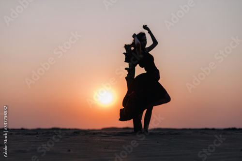 girl in the desert at sunset in a red dress developing in the wind © Denis