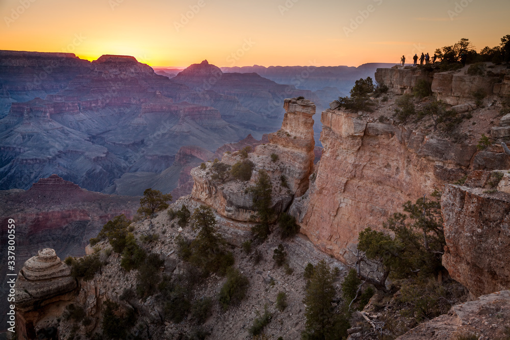 Sun sets over the Grand Canyon as silhouettes of people overlook from afar