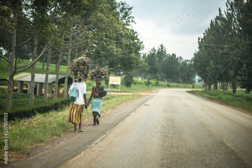 Women carry heavy load on head along African village road