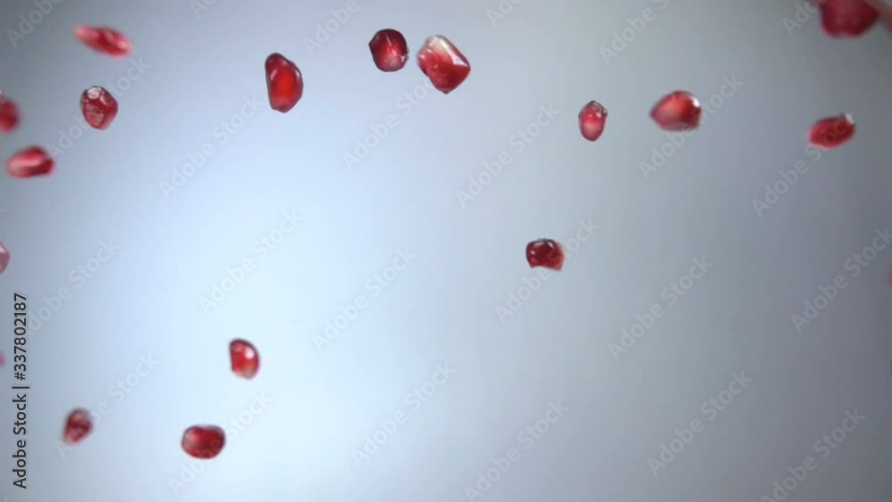 Juicy grains of ripe pomegranate are falling diagonally on the white background in slow motion Juicy grains of ripe pomegranate are falling diagonally on the white background in slow motion