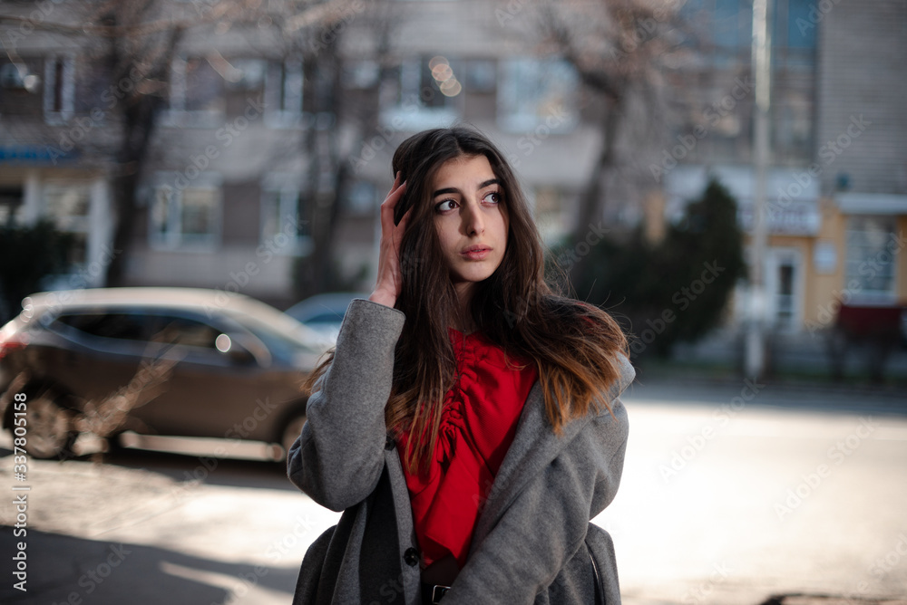 Girl in a red blouse and a gray cardigan on a blurry city background in early spring Girl in a red blouse and a gray cardigan on a blurry city background in early spring