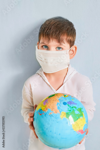 Caucasian boy in a medical mask holds a syringe with a vaccine in his hand and vaccinates the inflatable ball in the globe to prevent the virus epidemic. White background. Copyspace