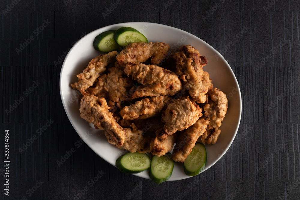 Fried Chicken with Cucumbers on a white plate on a dark background Fried Chicken with Cucumbers on a white plate on a dark background