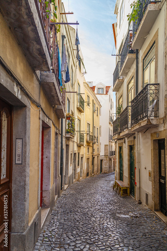 Old residential buildings along an empty, narrow and idyllic cobblestoned alley (Rua do Salvador) in the Alfama district in Lisbon, Portugal, on a sunny day.