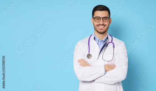 Horizontal banner of handsome doctor, showing confident smile, ready to help patients with health problems, isolated on blue background with copy space on left