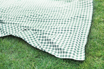 Blue checkered picnic cloth on green grass background,empty space food advertisement backdrop.