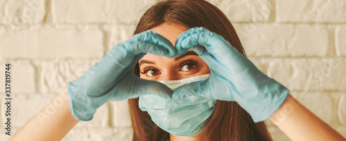 Banner young woman in protective face mask and medical gloves gesturing love shape sign. Happy girl in medical face mask and gloves looking through hands in form of heart symbol. Health care, COVID-19