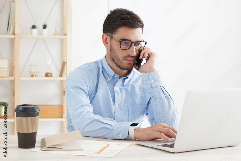 Business man with serious face solving problems while answering phone call, typing on laptop in office, looking uneasy and concerned Business man with serious face solving problems while answering phone call, typing on laptop in office, looking uneasy and concerned