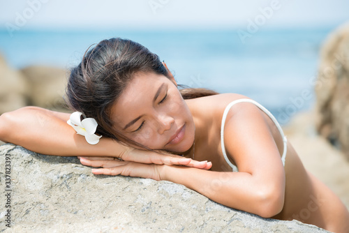 Beautiful Asian girl with frangipani flower in the hair resting outdoors at the infinity pool. Copy space.